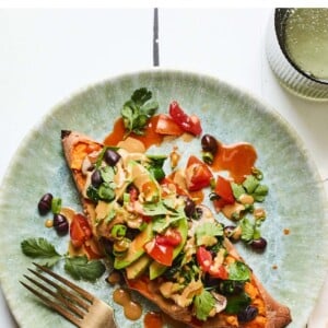 Black bean stuffed sweet potato on a plate with a fort and topped with tahini sauce, avocado, tomatoes and cilantro.