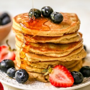 Stack of almond flour pancakes served with berries and maple syrup being drizzled on.