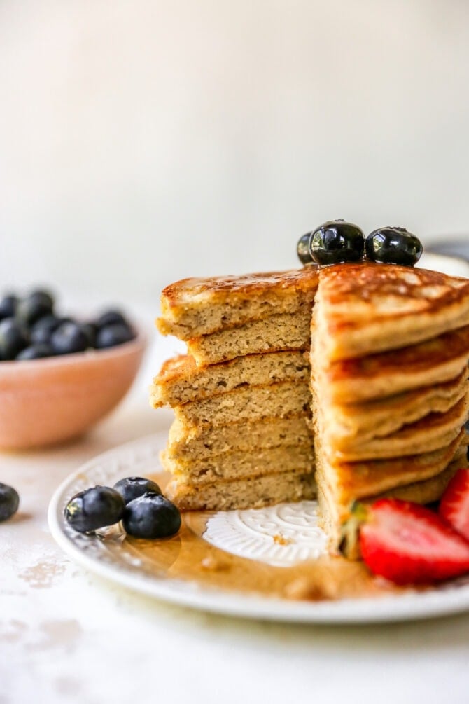 Stack of almond flour pancakes served with berries and maple syrup. A slice is taken out of the pancake stack.