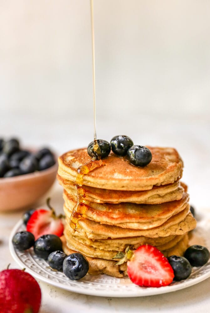 Stack of almond flour pancakes served with berries and maple syrup.