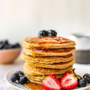 Stack of almond flour pancakes served with berries and maple syrup.