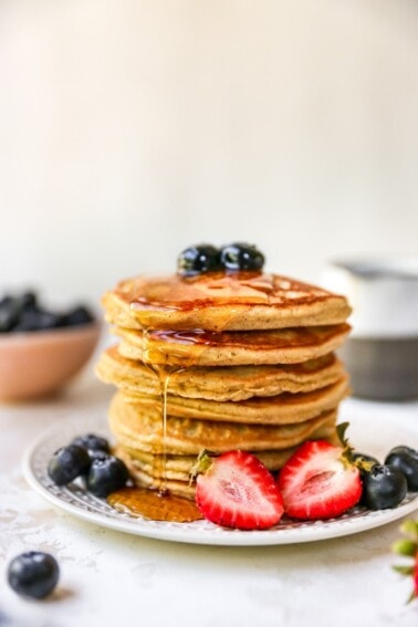 Stack of almond flour pancakes served with berries and maple syrup.