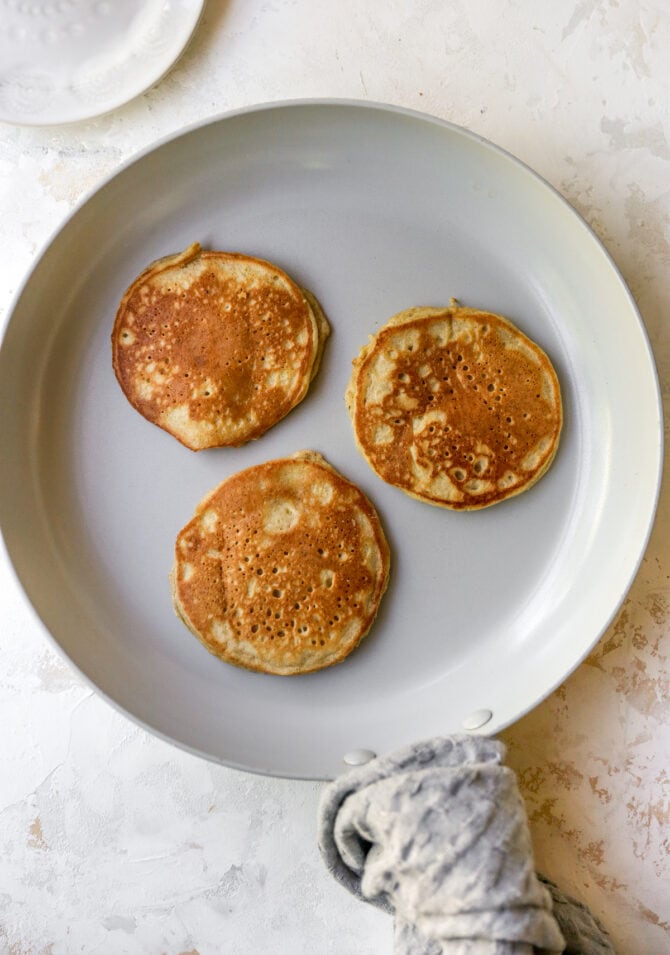 Three almond flour pancakes in a frying pan.