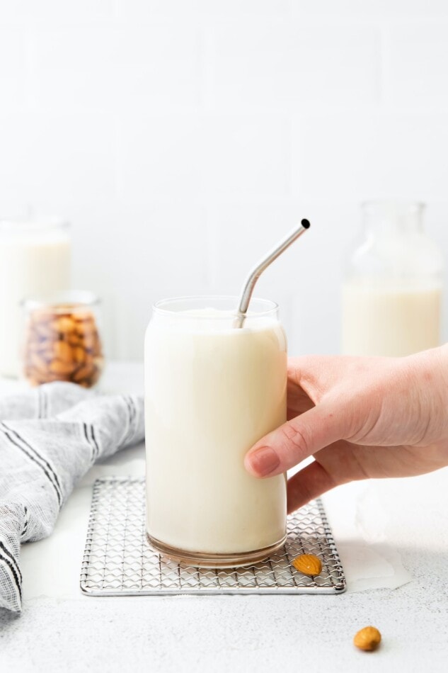 Hand holding a glass of almond milk with a metal straw.