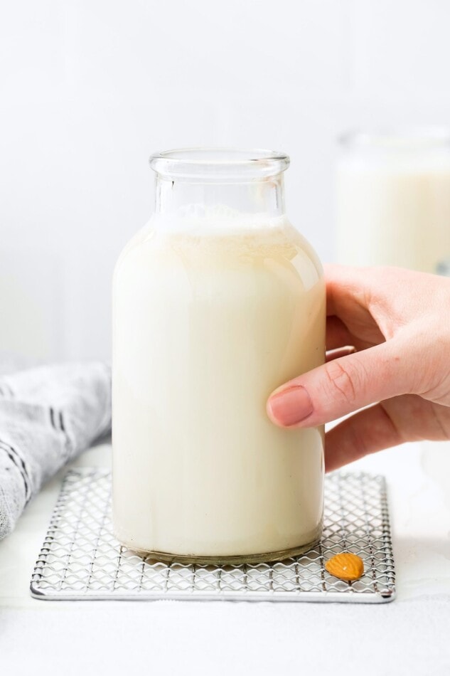 Hand holding a glass jar full of almond milk.