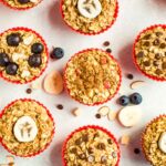 Muffin liners with baked oatmeal cups 4 ways. ingredients are surrounding them on the table like chocolate chips, blueberries, and apple chunks.