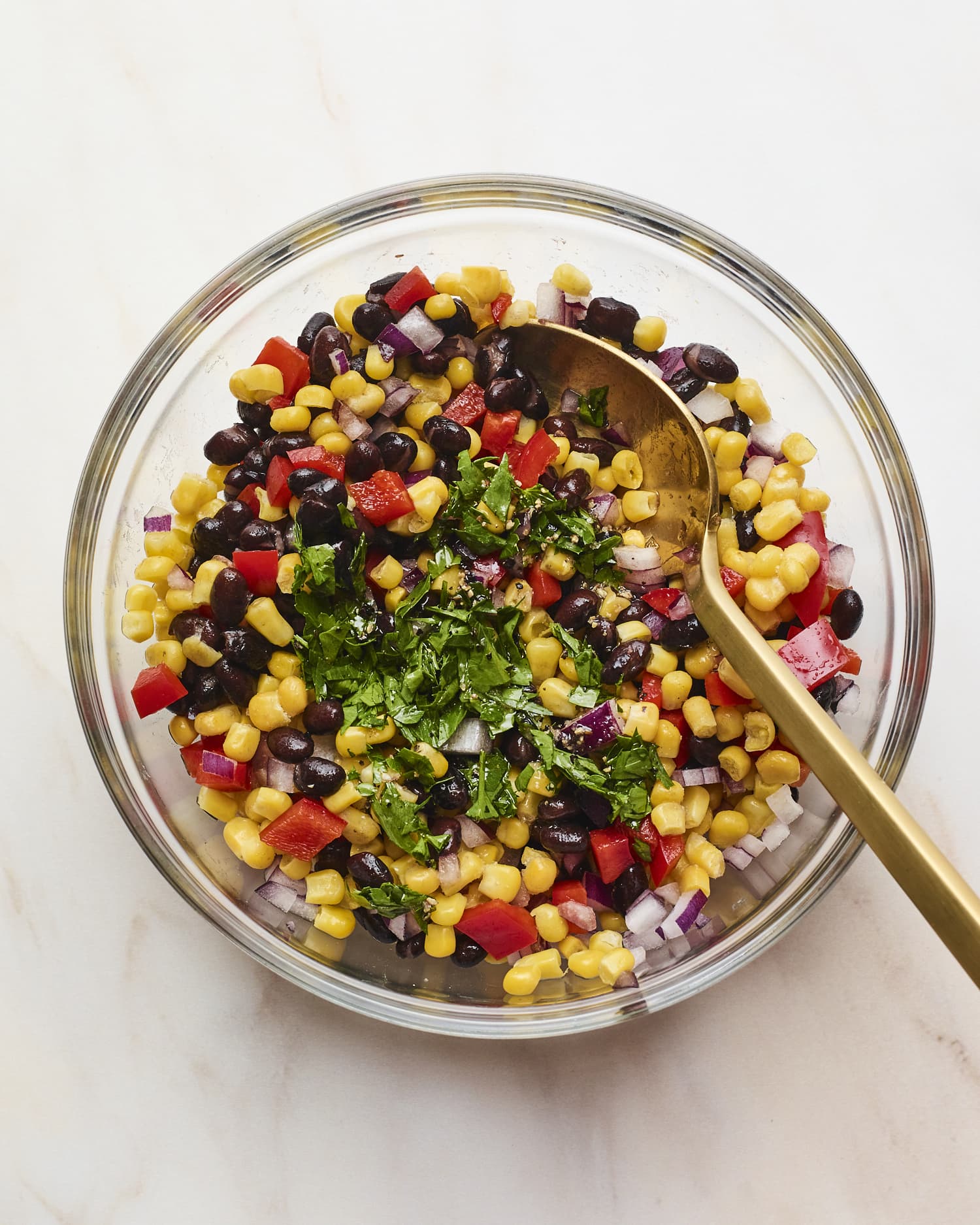 Mixing bowl with black bean and corn salad with a spoon and topped with cilantro.