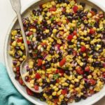 Serving bowl with black bean and corn salad. Spoon is in the bowl.