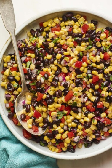 Serving bowl with black bean and corn salad. Spoon is in the bowl.