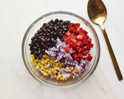 Mixing bowl with chopped pepper, onion, corn and black beans before being mixed.