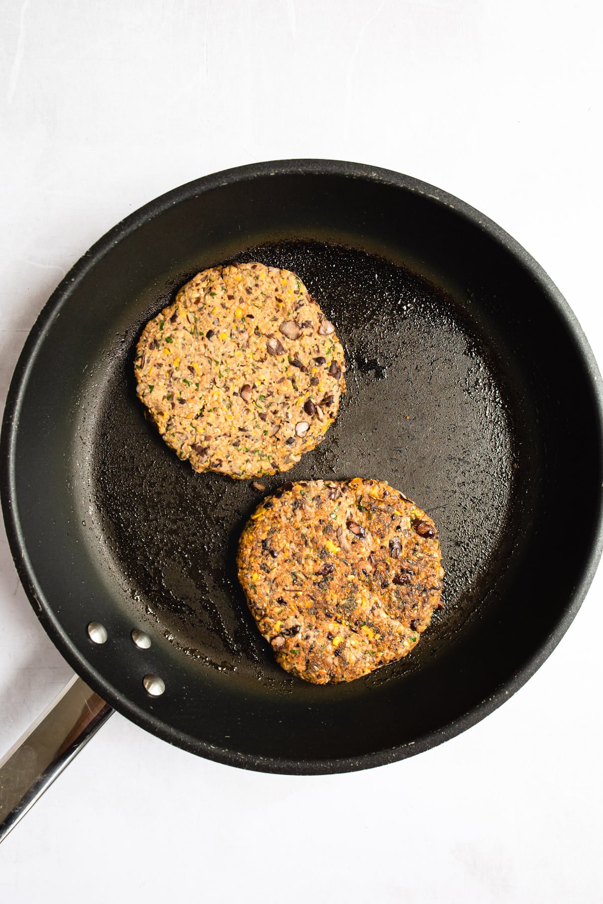 Two black bean burgers frying in a pan.