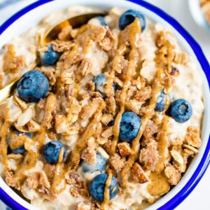 Blueberry overnight oats in a white bowl with blue rim. Topped with blueberries, crumble and nut butter.