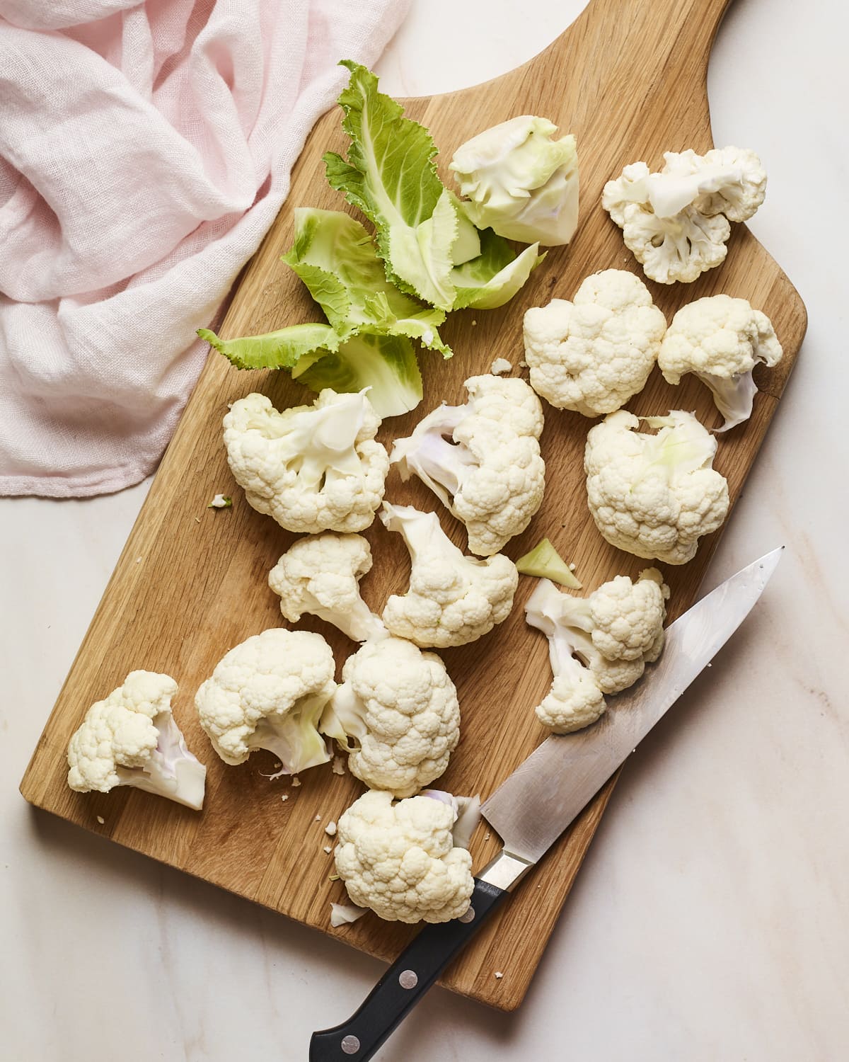 Cauliflower florets on a wood cutting board with a knife.