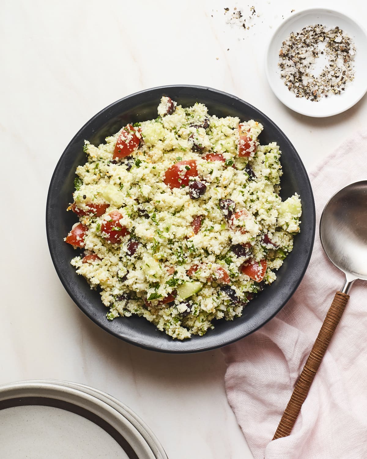 Serving plate with cauliflower tabbouleh. Salt and pepper and a serving spoon are beside the plate.