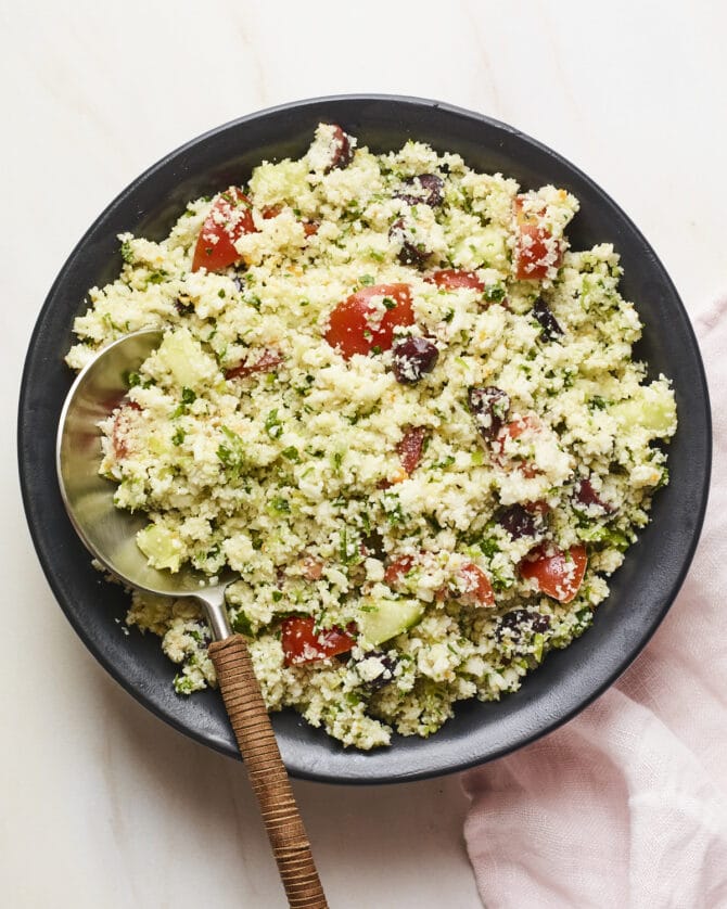 Serving bowl of cauliflower tabbouleh with a serving spoon.