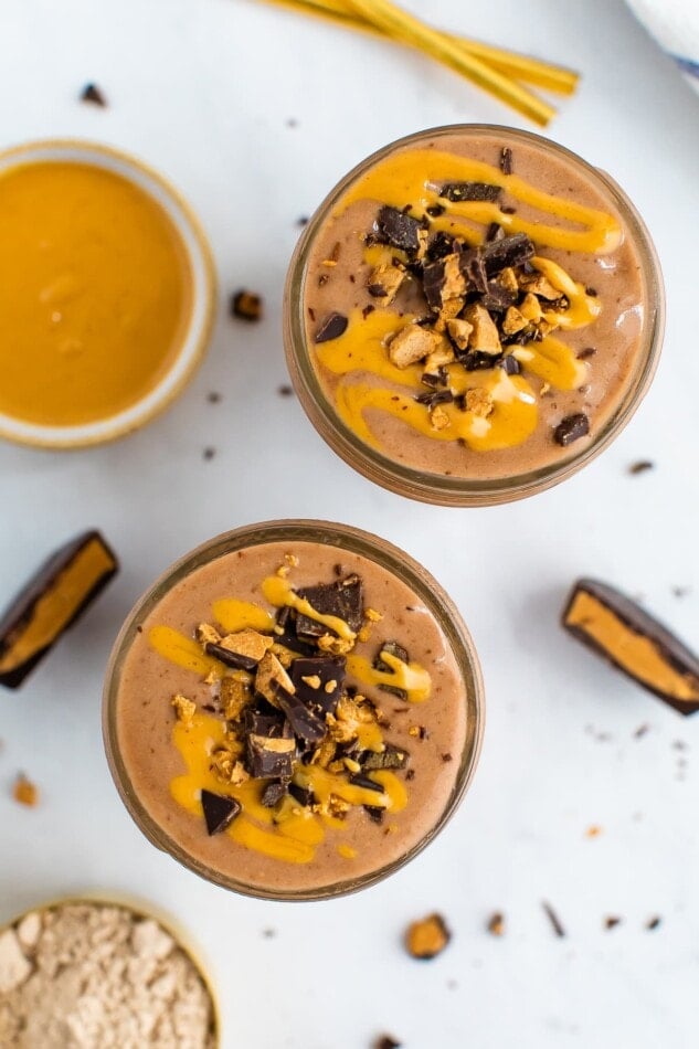 Two glasses of chocolate peanut butter smoothies, topped with peanut butter drizzle and chopped peanut butter cup.