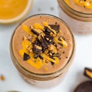 Chocolate smoothie with peanut butter drizzle and chopped peanut butter cup on top.