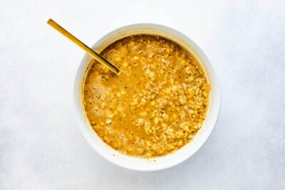 Ingredients to make coffee overnight oats in a bowl all mixed together with a gold spoon.