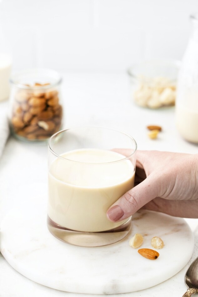 Hand holding a glass of macadamia milk.