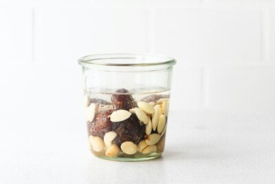 Glass jar with almonds, macadamia nuts and dates soaking in water.