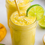 Two glasses with avocado mango smoothie garnished with coconut and lime slices.