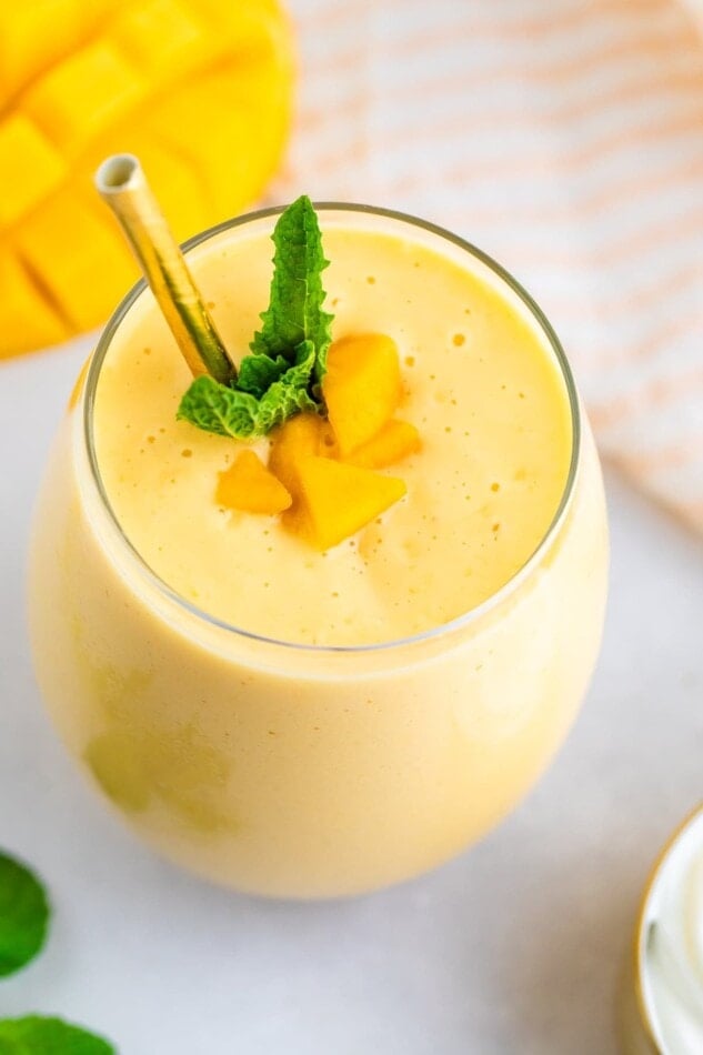 Mango smoothie in a glass with a metal straw and garnished with mint and mango chunks.
