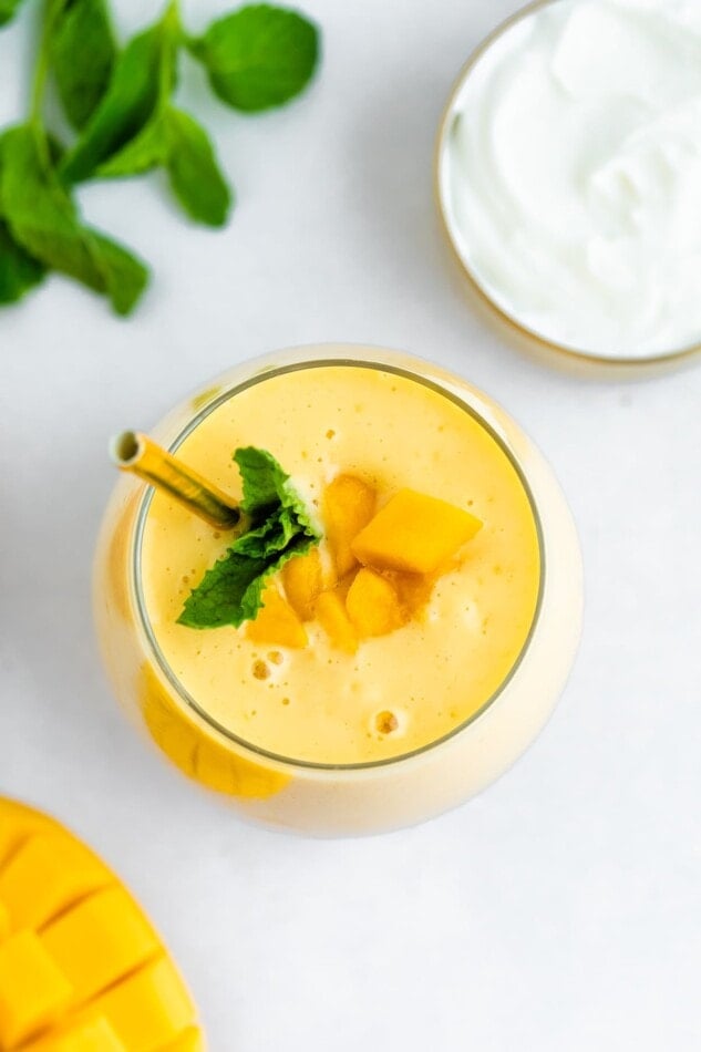 Mango smoothie in a glass with a metal straw and garnished with mint and mango chunks.