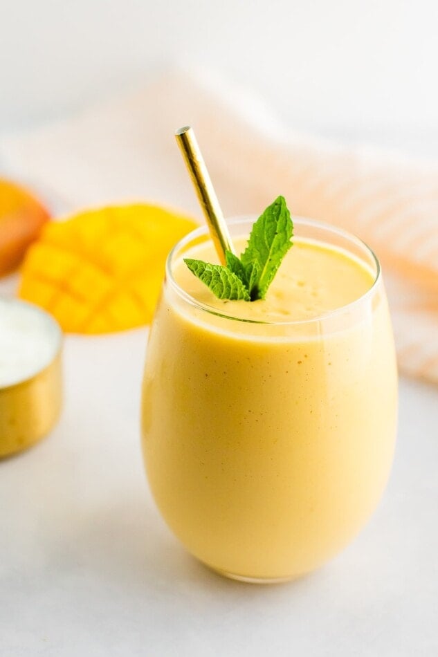 Mango smoothie in a glass with a metal straw and garnished with mint.