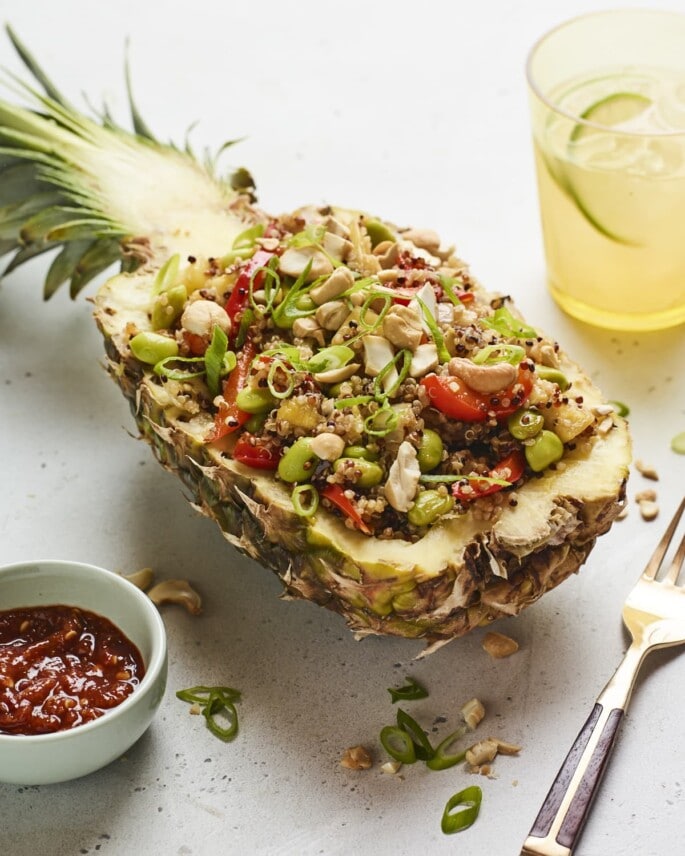 Pineapple boat full of pineapple fried quinoa. Bowl of garlic chili sauce is next to the pineapple.