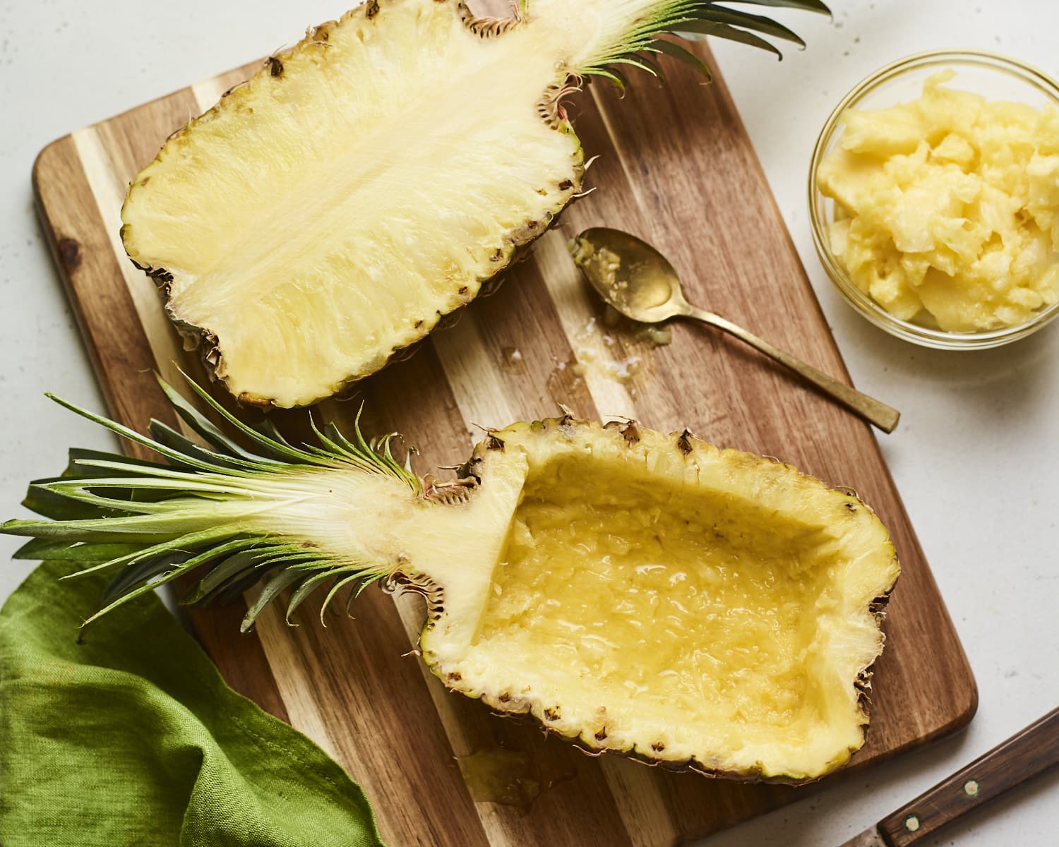 Two halves of pineapple on a cutting board. One half is scooped out.