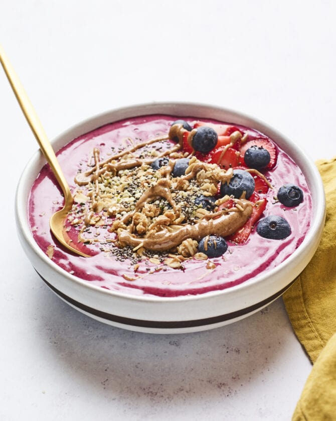 Smoothie bowl topped with berries, granola and almond butter. Spoon is in the smoothie bowl.