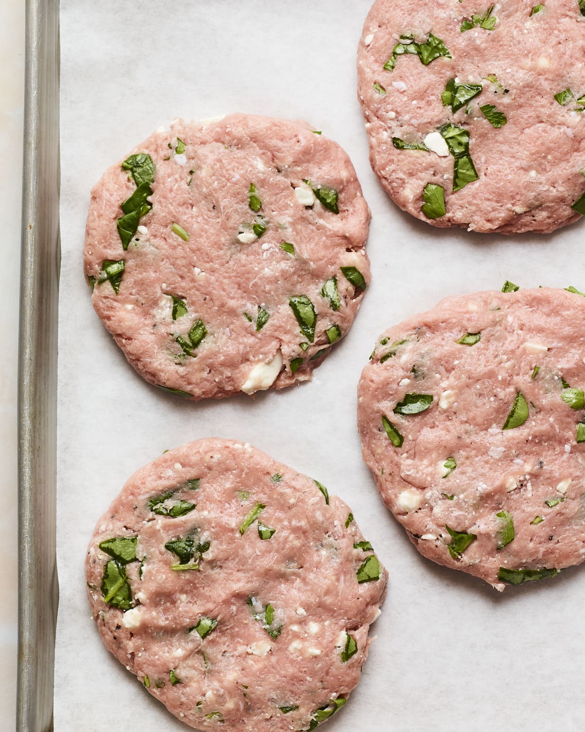 Four spinach and feta turkey burger patties on a sheet pan.