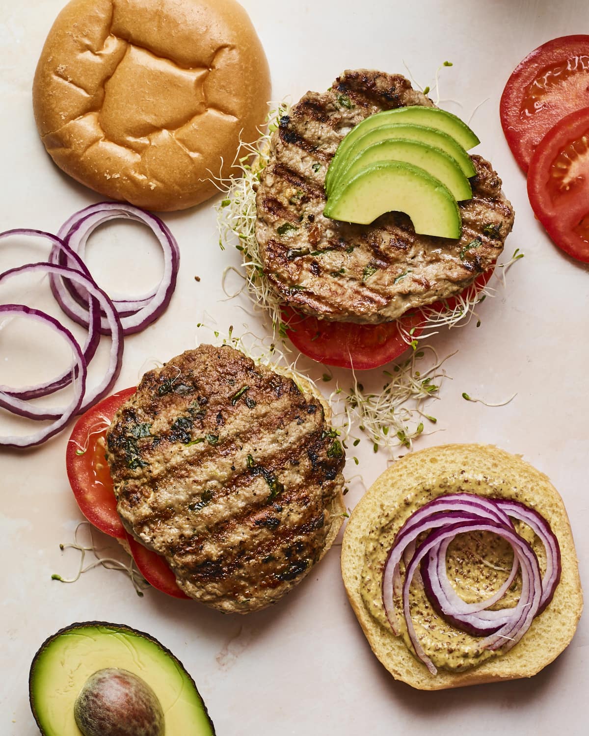 Two open faced spinach and feta turkey burgers with burger toppings and buns around on the table.