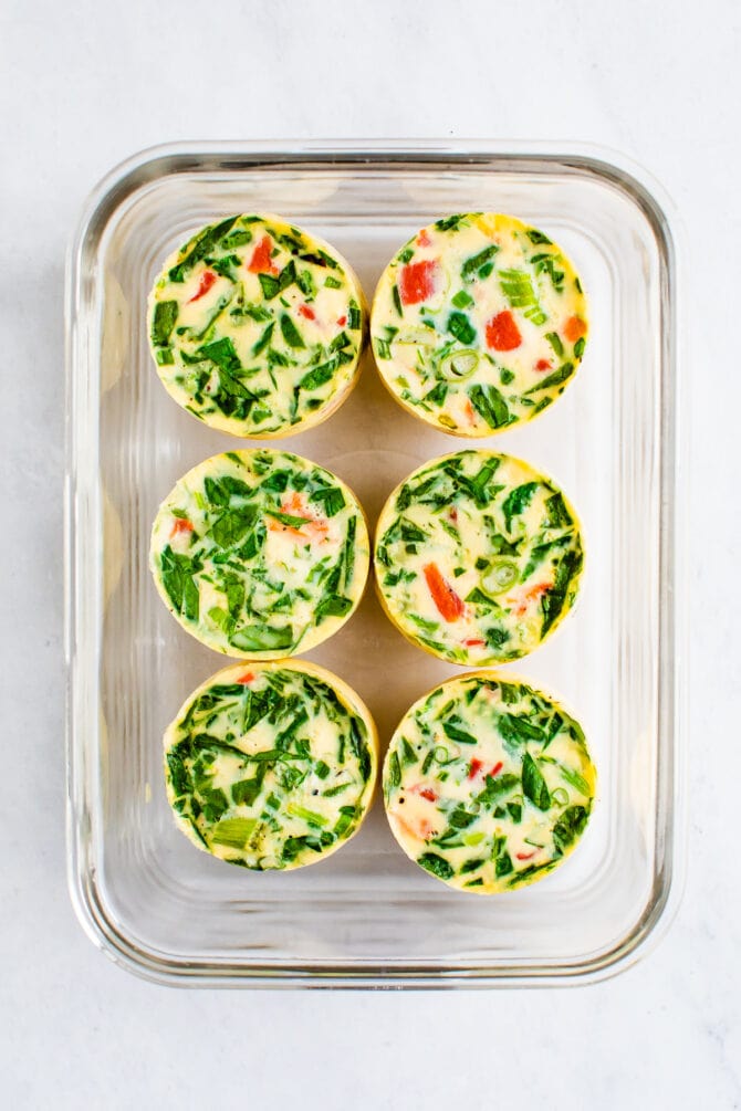 6 egg white bites made with spinach and red pepper in a glass food storage container.