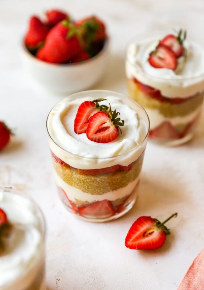 Strawberry, yogurt and quinoa parfaits, layered in a two glasses. A bowl of strawberries is behind the two parfaits.