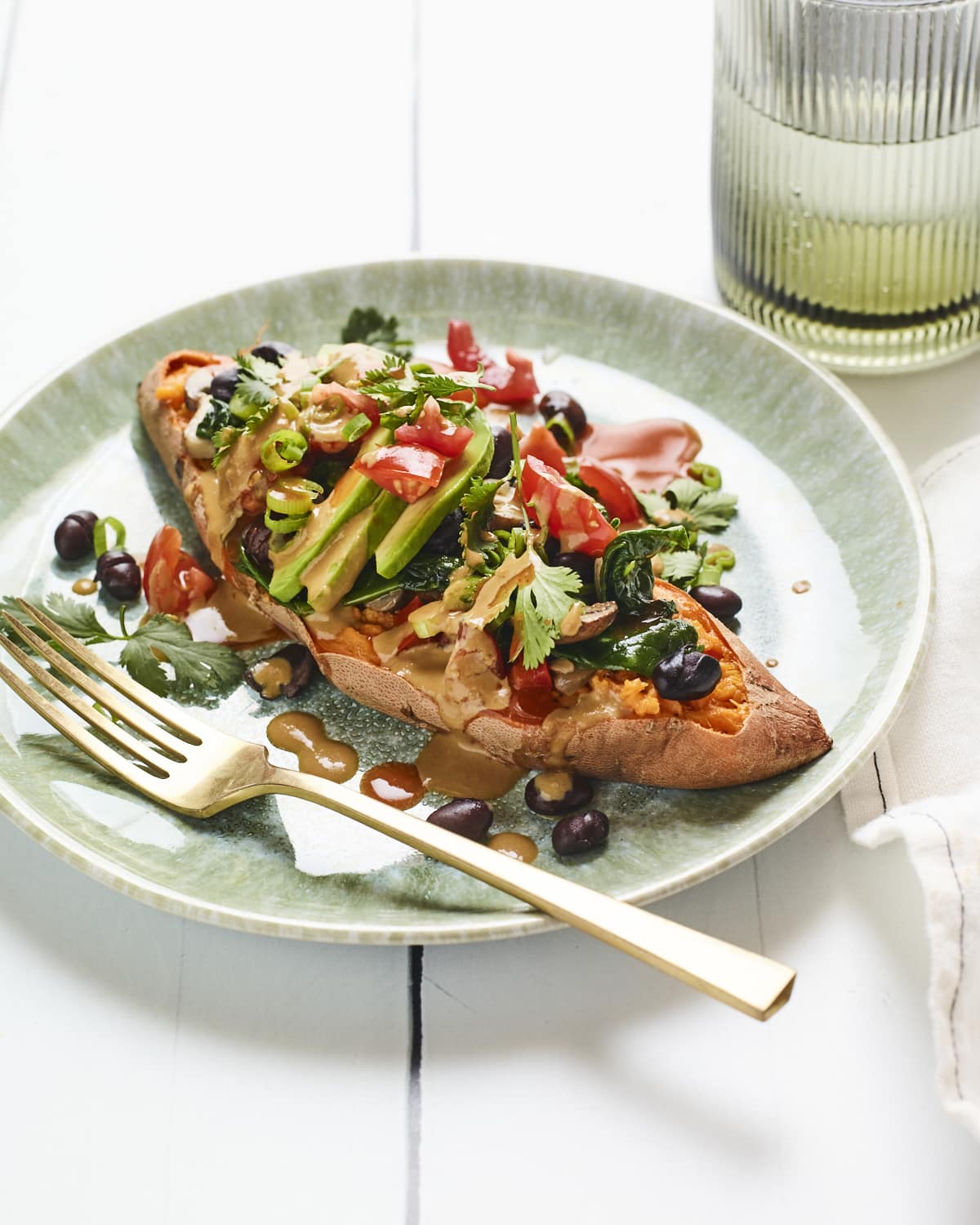 Black bean stuffed sweet potato on a plate and drizzled with tahini sauce.