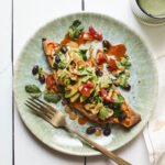 Black bean stuffed sweet potato on a plate and drizzled with tahini sauce. Topped with cilantro, tomatoes and avocado.