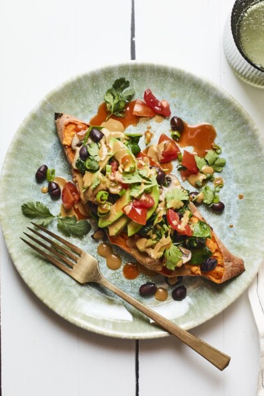 Black bean stuffed sweet potato on a plate and drizzled with tahini sauce. Topped with cilantro, tomatoes and avocado.