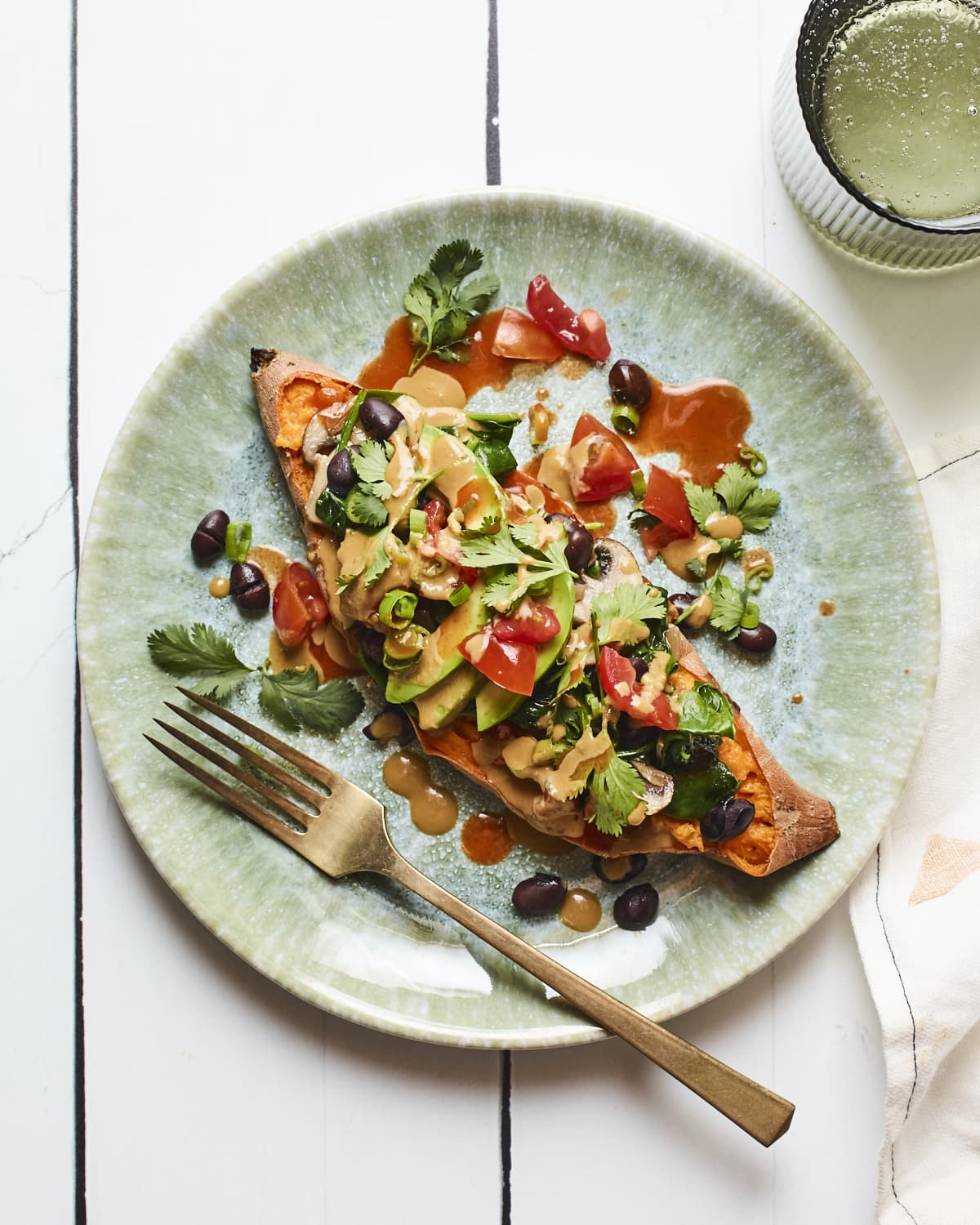 Black bean stuffed sweet potato on a plate and drizzled with tahini sauce. Topped with cilantro, tomatoes and avocado.