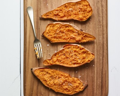 Four sweet potato halves on a wood cutting board.