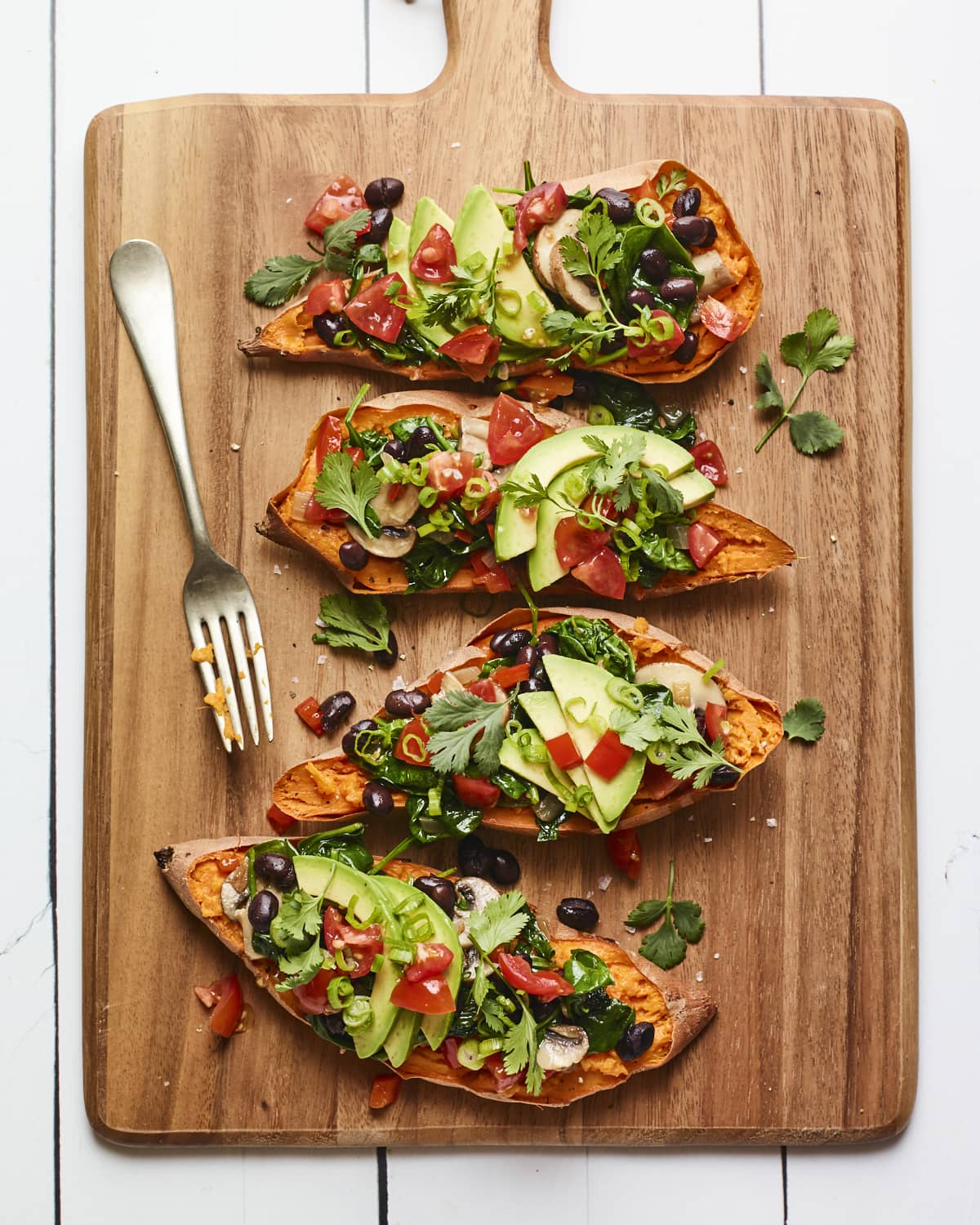 Four black bean stuffed sweet potatoes on a wood cutting board.