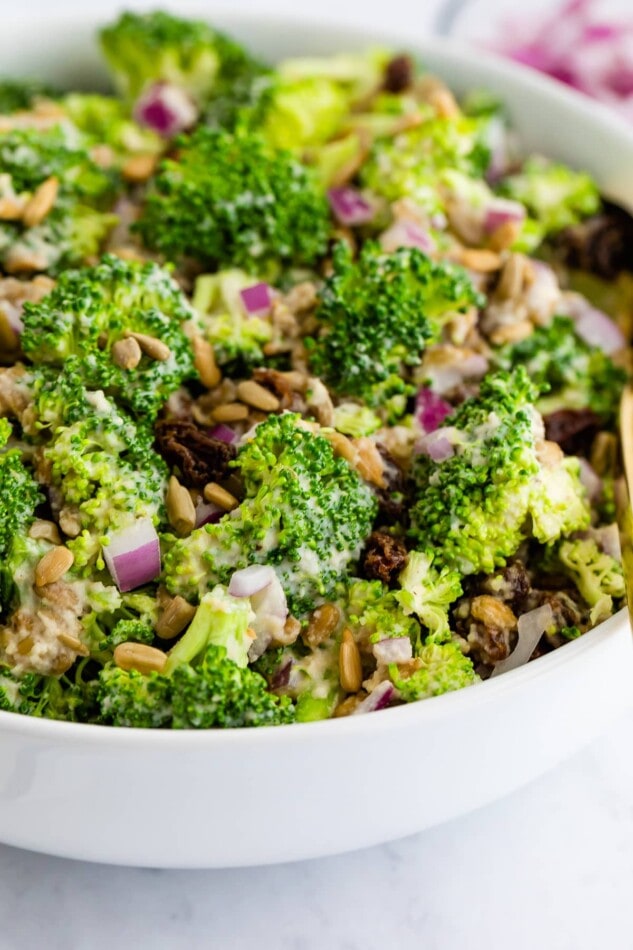 Side angle view of vegan broccoli salad in a white bowl.