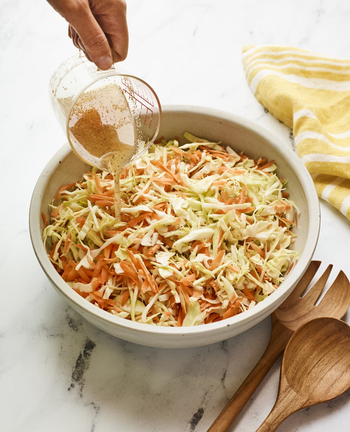 Person pouring apple cider vinegar dressing over a serving bowl of coleslaw.