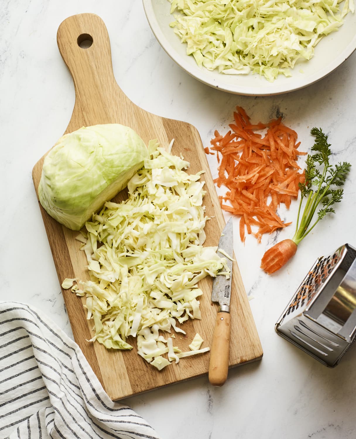 Cutting board with chopped cabbage and grated carrot.