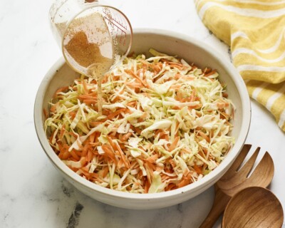 Pouring apple cider vinegar dressing over a serving bowl of coleslaw.