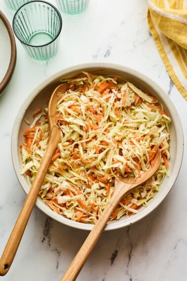 Serving bowl of apple cider vinegar coleslaw with wood serving spoons.