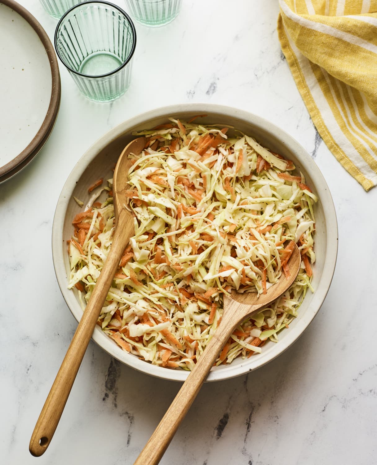 Serving bowl of apple cider vinegar coleslaw with wood serving spoons.