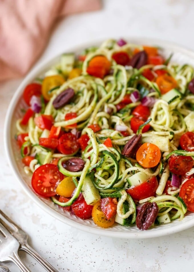 Serving bowl of zucchini noodle salad with tomatoes, peppers and olives.