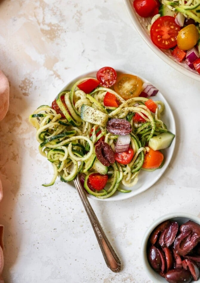 Plate of zucchini noodle salad with tomatoes, peppers and olives.