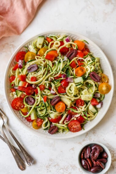 Serving bowl of zucchini noodle salad with tomatoes, peppers and olives.